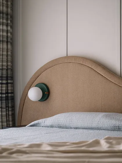 A close-up of the guest bed, showing the custom-designed globe sconce. The mix of textures, from the upholstered headboard to the plaid curtains, creates a cozy and inviting feel.