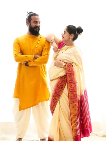 A stylish and traditional couple's portrait. The mom-to-be's elegant saree and the dad-to-be's bright kurta create a beautiful contrast against the minimalist white background.