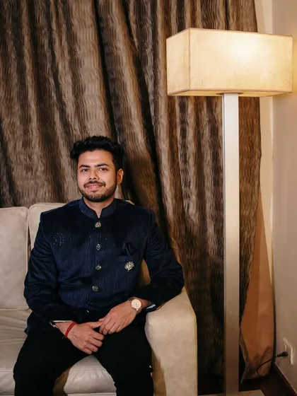 A handsome portrait of the groom seated and relaxed before the ceremony. The warm indoor lighting creates a comfortable and intimate atmosphere.
