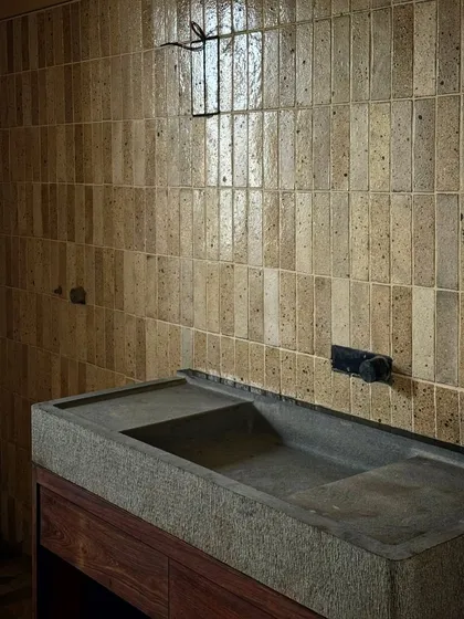 The interior of a bathroom in the Kamshet farmhouse, featuring a custom-carved stone sink and vertically laid tiles. We pay close attention to the details and textures of even the most private spaces.