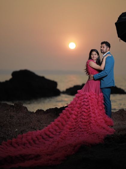 A beautiful pre-wedding portrait on the rocks at sunset. The pink ruffled trail gown is the perfect choice for a romantic and dramatic beach shoot.