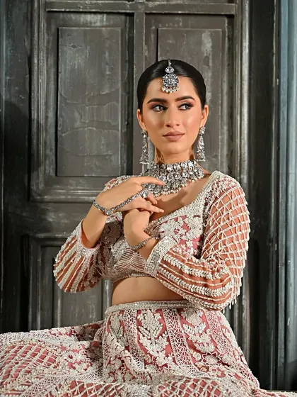 A seated portrait showing the complete look. The polished low bun adds a regal touch to the heavily embroidered lehenga.