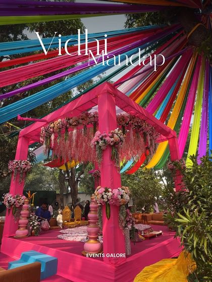 Another view of the stunning Vidhi Mandap, showcasing the beautiful contrast between the bright pink structure and the multi-colored canopy, creating a joyful and celebratory atmosphere.
