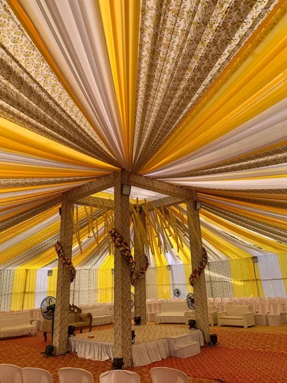 A grand mandap setup for a Haldi ceremony, created entirely with fabric drapes. The canopy of yellow, white, and brown printed fabric creates a spectacular visual from below.