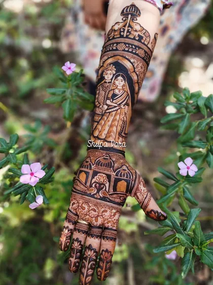A full arm bridal design telling a story. This piece features a couple portrait on the upper arm and a detailed jharokha design on the hand.