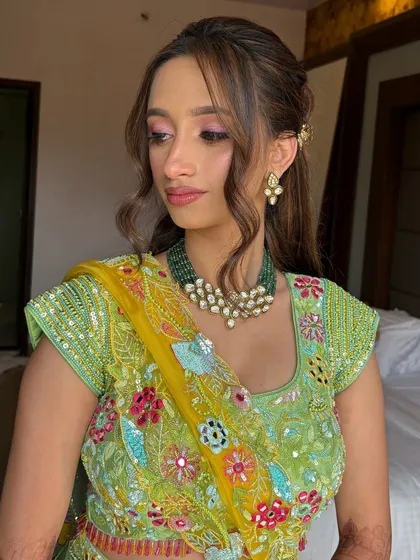 The bride's fresh and pretty Haldi look is completed with a simple yet elegant half-updo and face-framing tendrils.