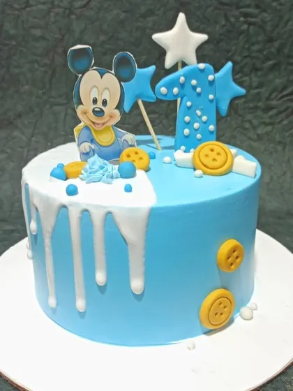 A cute Mickey Mouse cake for a first birthday. The blue cake features a white drip effect and is decorated with button and star accents.