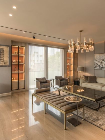 An elegant living space featuring polished marble floors, a statement chandelier, and a neutral color palette. Backlit display cabinets and curated artwork add a personal touch, while large windows fill the room with natural light.