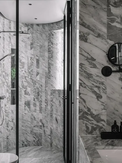 Luxury and function meet in this master bathroom, where we used vertical stripes of Statuario marble to create a curved shower wall. This technique adds a soft, sculptural feel to the space, which is unified by a sophisticated grey scale palette. The design demonstrates how we carry a home's core architectural theme through to its most private areas.