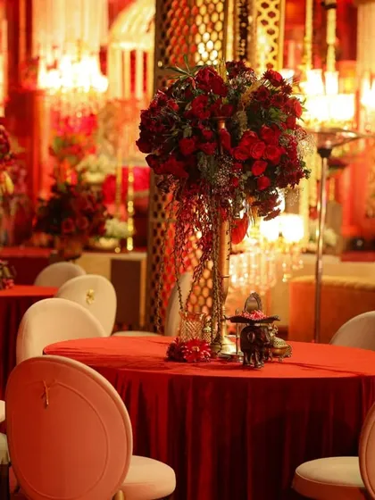 For this regal wedding, the guest tables were styled with tall, dramatic centerpieces of red roses, set against the warm glow of chandeliers and intricate gold lattice screens.
