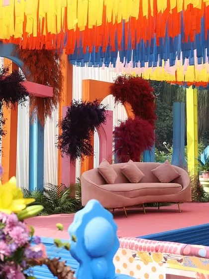 The main stage for a colorful Haldi, featuring a pink sofa and a backdrop of geometric shapes and dark, moody florals.