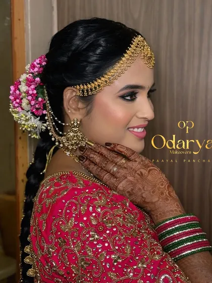 A beautiful side profile showcasing the harmony between the makeup, the intricate matha patti, and the floral bridal bun. The bold cat-eye makeup adds a touch of modern glamour to this traditional look.