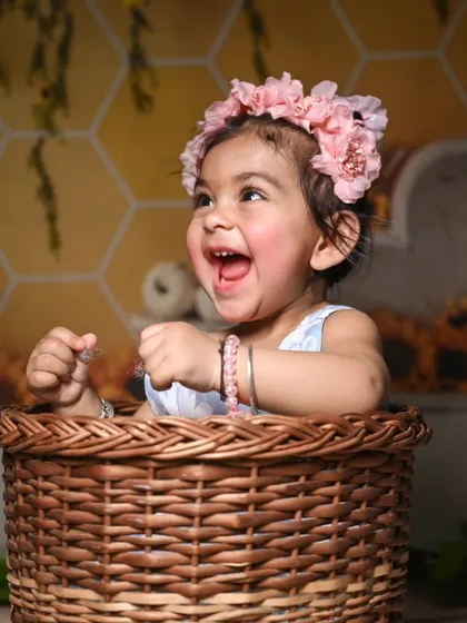 Capturing pure joy during a pre-birthday shoot. The backdrop features a honeycomb pattern with sunflowers, complemented by a rustic wicker basket prop, creating a warm and cheerful setting for baby photos.