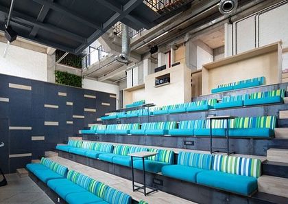 The Communique office includes a large, tiered seating area for company-wide meetings and presentations. The vibrant, colorful upholstery adds a playful touch to the industrial-inspired space.