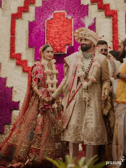 The couple walks hand-in-hand, a picture of unity and happiness. The grand floral backdrop adds a vibrant, celebratory feel to this candid moment during the ceremony.
