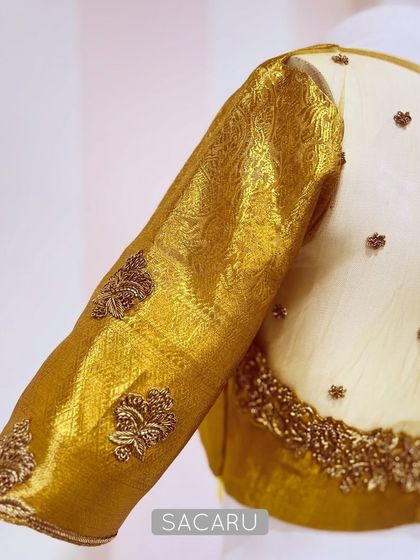 A detailed shot of the gold tissue blouse, focusing on the sheer back panel adorned with scattered embroidery and the rich texture of the brocade sleeve.