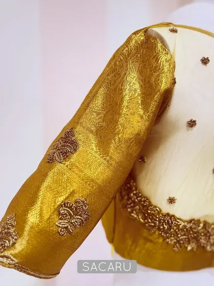 A detailed shot of the gold tissue blouse, focusing on the sheer back panel adorned with scattered embroidery and the rich texture of the brocade sleeve.