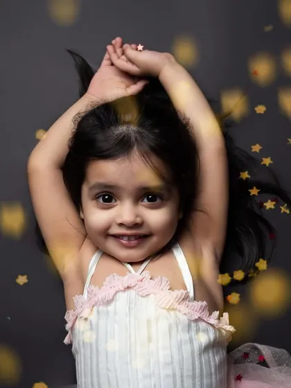 A magical portrait of a little girl surrounded by sparkling glitter. The dark background makes her and the golden stars truly pop.