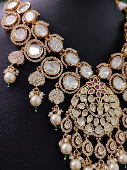 A close-up of the necklace's pendant, showcasing the intricate arrangement of kundan stones and the central ruby-colored stone.