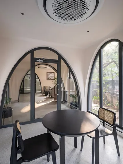 A quiet seating nook in the ARCUS residential building in Chennai, framed by distinctive catenary arches. This design choice was a creative interpretation of traditional forms, used to define spaces and flood them with natural light. The arches create a visual dialogue between the interior and the lush, tree-lined exterior.