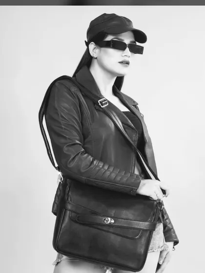 A cool, edgy shot of a model in a black leather jacket, denim shorts, and sunglasses, holding a handbag. The black and white treatment gives it a timeless, high-fashion feel.