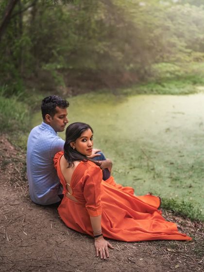 A couple sits by a mossy green pond, the woman looking back over her shoulder. This outdoor shot has a storybook quality, with the lush scenery creating a romantic and slightly mysterious backdrop.