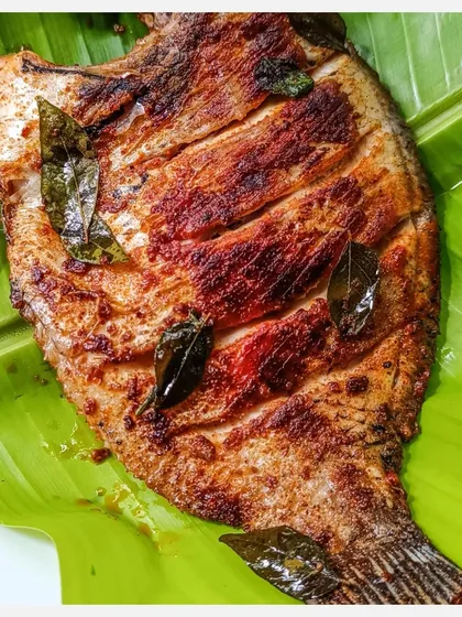A close-up of the Tawa Grilled Karimeen, showing the perfect char and the fragrant curry leaves.