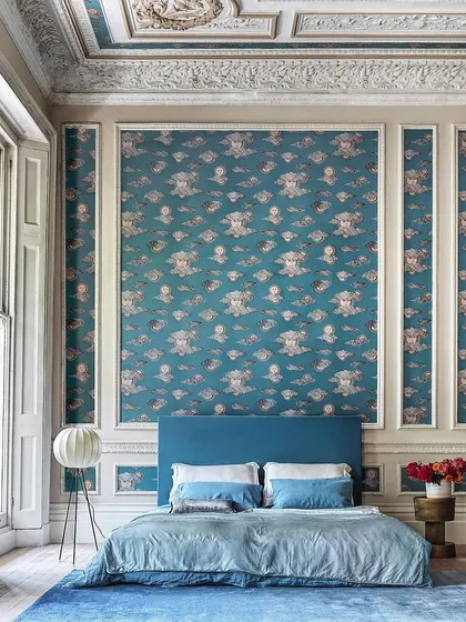 Inspired by a 1950s Piero Fornasetti print, this Cole & Son wallpaper pairs personified suns with stylized architecture. The design adds a unique and whimsical charm to this grand bedroom, even extending to the ceiling.