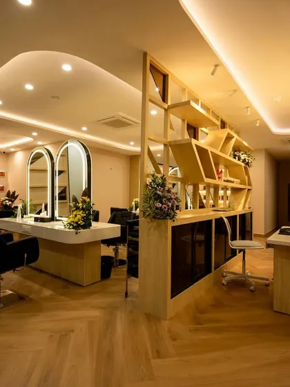 This wide-angle view captures the salon's main floor, showcasing the seamless flow between the reception and styling areas. We designed the custom geometric shelving unit as a functional art piece, complemented by soft, layered ceiling lights to create a warm and sophisticated ambiance.