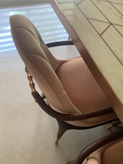 A detail of a dining chair, showing the elegant curve of the wooden armrest and the soft, quilted upholstery.