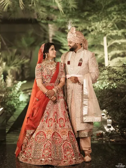 A timeless portrait of the bride and groom against a lush, green backdrop. Her red lehenga and his elegant sherwani create a stunning contrast.