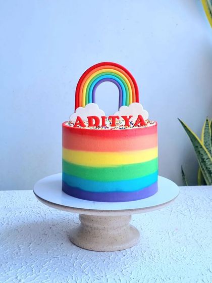 A full view of the buttercream rainbow cake on its stand.