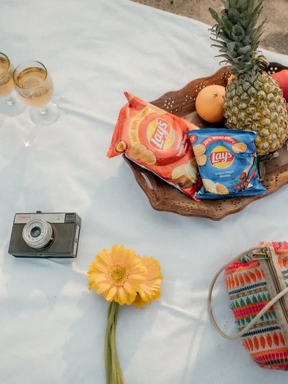 A flat-lay of the picnic setup, including a vintage camera, fruits, snacks, and flowers. This shot helps to set the scene and theme for their romantic beach date.