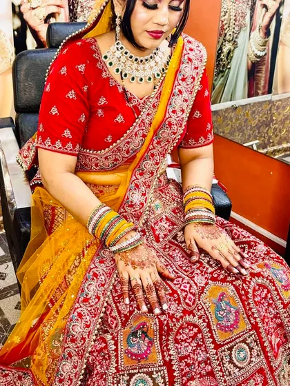 A bride seated and ready for her ceremony. Her makeup is done to complement her red and yellow lehenga, with a focus on traditional elements.