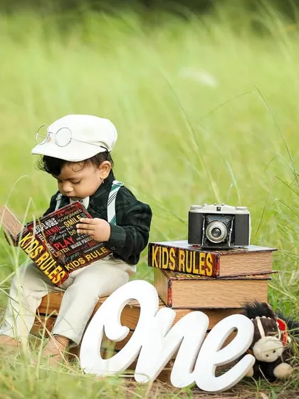 A vintage-themed outdoor first birthday shoot, with the little one dressed in a cap and suspenders, reading a book.