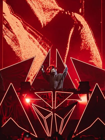 Alan Walker hypes up the crowd from his custom DJ booth, with red lights and visuals creating a dramatic effect.