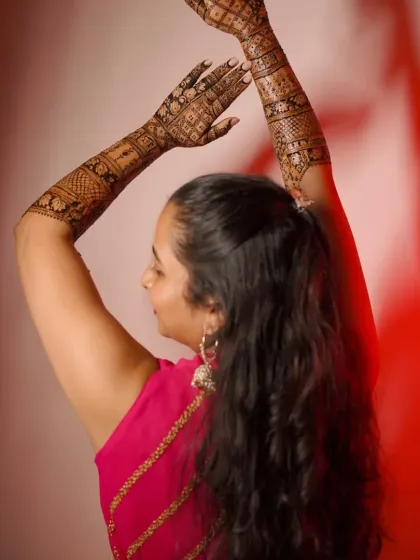 A beautiful pose from a client, showcasing her full-arm mehndi. The design looks stunning against the red background.