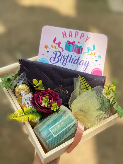 A simple and sweet birthday hamper designed for her. This gift includes a stylish wallet, Ferrero Rocher chocolates, a blueberry scented candle, and a bath loofah, all presented in a rustic wooden tray with a "Happy Birthday" card.