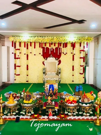 A baby shower setup in a home, featuring a backdrop of white and red flower garlands. The green turf for the plate display adds a touch of freshness.