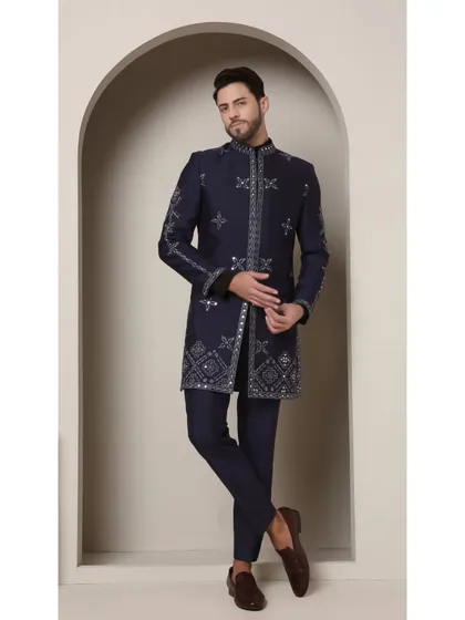The Neel Amber achkan in a deep, opulent navy. This handcrafted piece features intricate geometric patterns and mirrored embellishments for a look of timeless luxury.