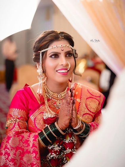 A beautiful over-the-shoulder shot of the bride with her hands in a respectful 'namaste'. Her expression is full of warmth and anticipation, captured during the wedding ceremony.