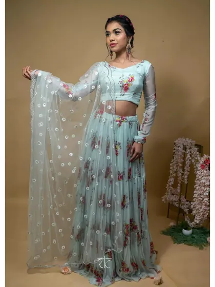 The model showcases the full baby blue floral lehenga set, holding the sheer, embroidered dupatta to display its full beauty. A light and enchanting choice.