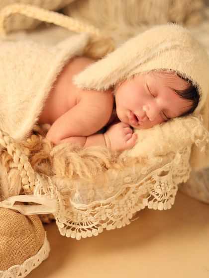 A close-up of the baby in a bunny hat, nestled in a basket with lace trim. The focus on soft, neutral textures creates a calm and gentle mood.