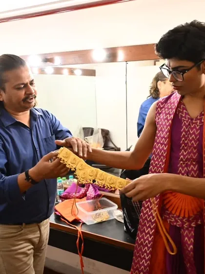 A senior student helps a junior dancer with his costume belt. These moments of mentorship are an important part of the learning process at Natya Vriksha, fostering a sense of responsibility and community.