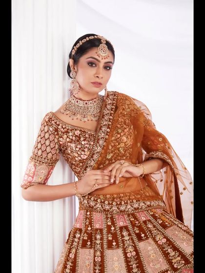 A model looking regal in a unique rust-colored bridal lehenga with intricate panel work. This is a great option for brides looking for something beyond traditional red.