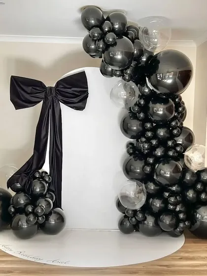 An elegant all-black balloon arrangement for a 29th birthday. The large black bow adds a touch of drama and sophistication to the monochrome backdrop.