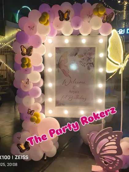 The entrance setup for the terrace party, featuring a personalized welcome sign framed with lights and a pastel balloon arch with butterfly accents.