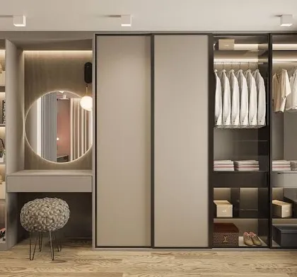 We design wardrobes that are more than just storage; they are personal styling zones. This custom walk-in unit features a mix of open shelving, glass-door cabinets for visibility, and a dedicated vanity nook with a round mirror, blending organization with pure elegance.