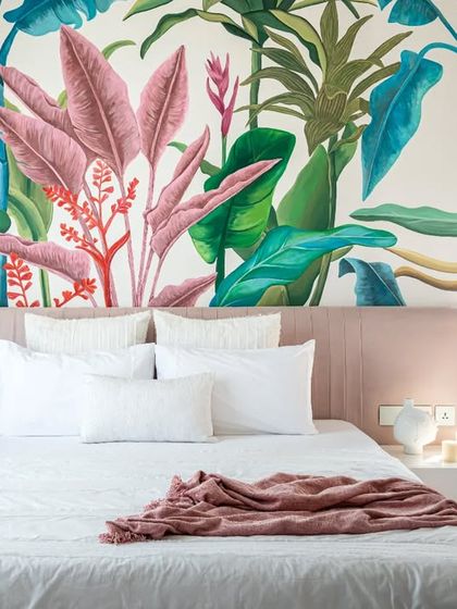 A tropical paradise for a bedroom, this hand-painted mural features vibrant, oversized botanicals in shades of pink and green. The artwork transforms the room into a serene and dreamy escape.