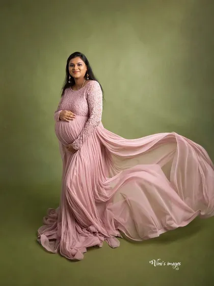 A classic maternity pose with a flowing pink gown. The wind-swept fabric adds drama and movement, highlighting the mother's graceful form against a simple olive green backdrop.